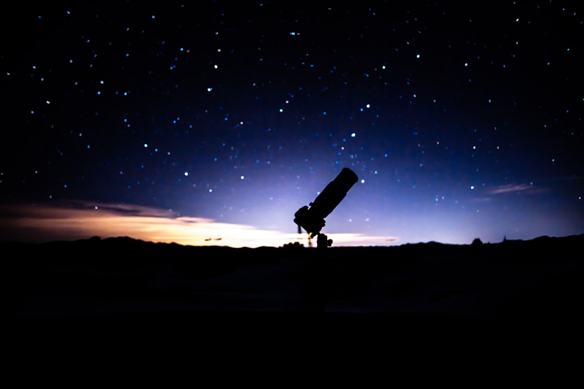 A telescope silhouetted on a hilltop under a starry sky